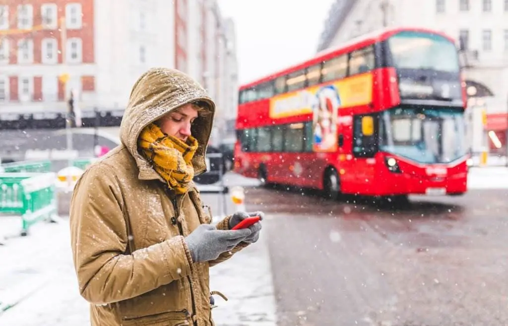 UK, London, young man standing next to the road in the city looking at cell phone - Weather in England During Winter - Planet Travel Advisor UK, London, young man standing next to the road in the city looking at cell phone - Weather in England During Winter - Planet Travel Advisor