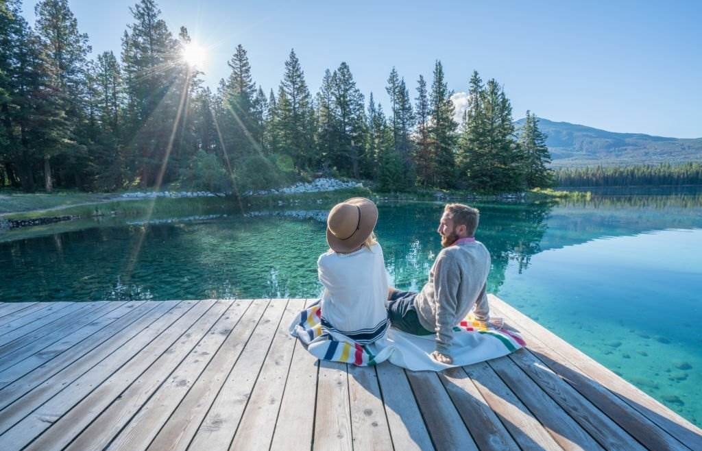 Cheerful Young Couple Sitting on Lake Pier and Sharing Some Relaxing Moments - Best Time to Visit Canada - Planet Travel Advisor