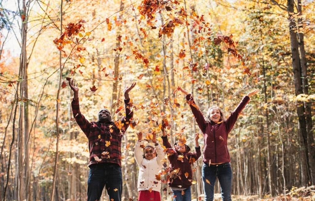 Mixed race family in a forest, throwing maple leaf, during autumn, Quebec, Canada - Best Time to Visit Canada - Planet Travel Advisor