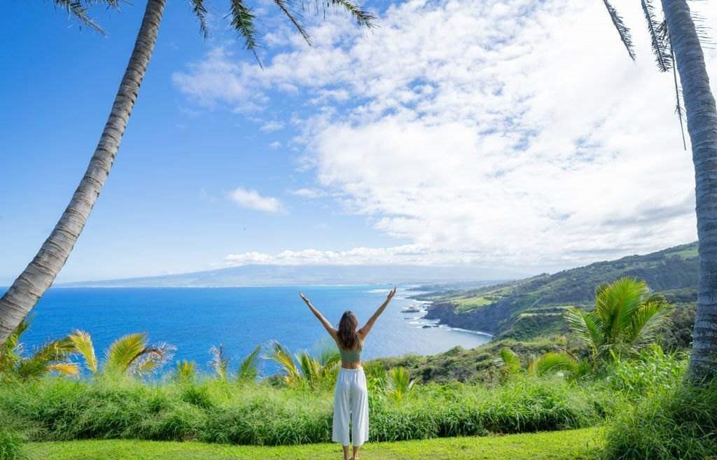 Is April Recommended to Visit Hawaii - Young woman relaxes at coastal viewpoint, over sea - Planet Travel Advisor